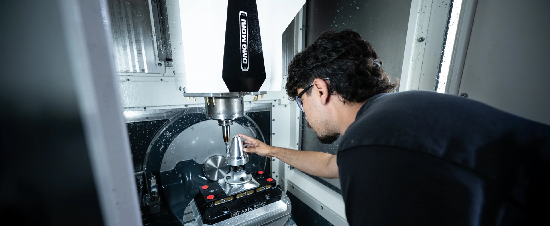 Machinist inspecting a precision component inside a DMG Mori CNC machine
